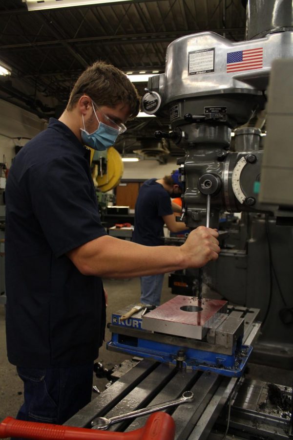 A student in the Precision Machining program uses a machine while wearing a mask.