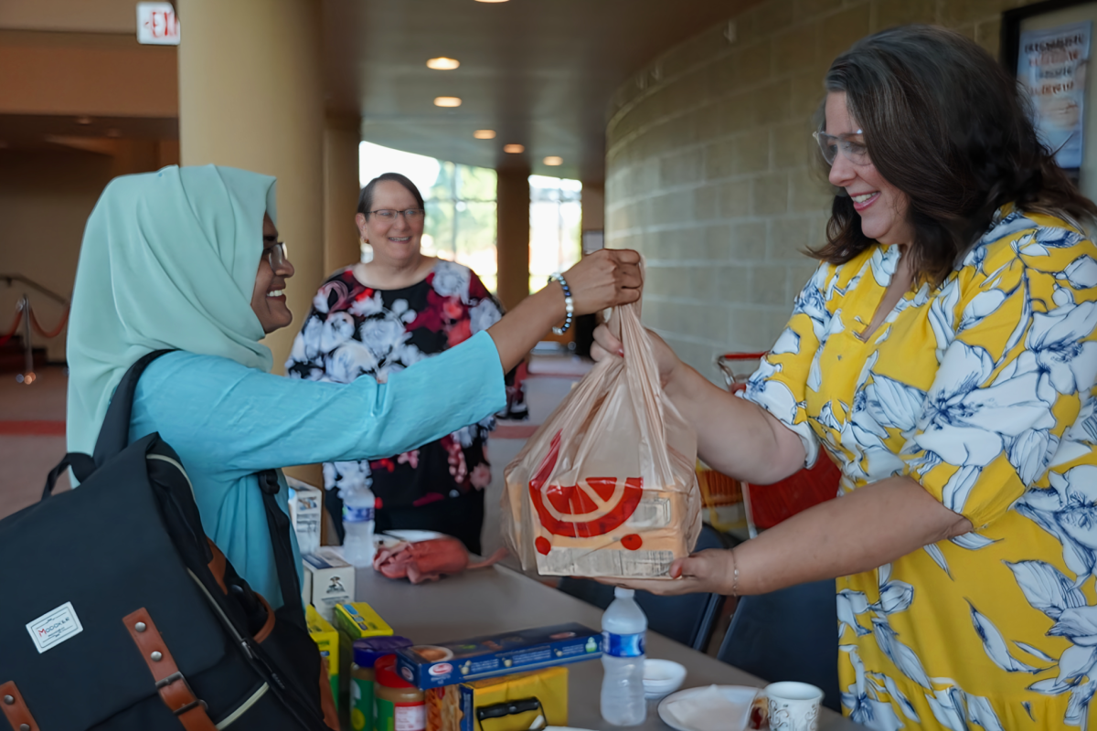 Professor Dr. Jannatul Ferdush hands items for the Sandy’s Pantry Donation Drive at Executive Director of VU Foundation and Senior Director of Institutional Advancement Kristi Deetz in the lobby of the Red Skelton Performing Arts Center during the university's opening meeting last month. 